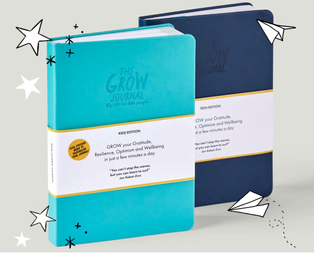 Two journals, one navy blue and one teal blue, on a grey background with some hand drawn stars and paper planes illustrated on top of the journals. Both journals have an embossed 'Grow' Journal title and a white paper band around the middle with text talking about how to use the journal.